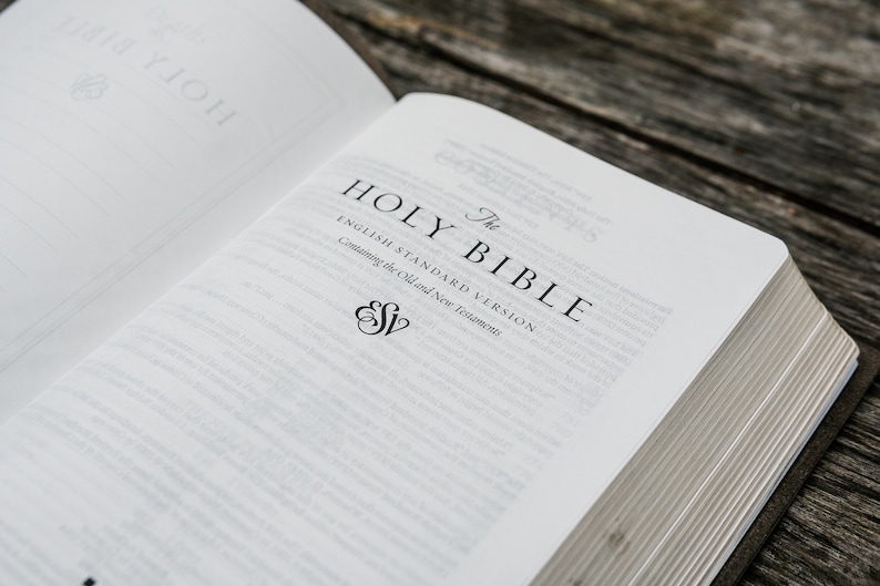Puede incluir: Primer plano de una Biblia abierta con el t&iacute;tulo "The Holy Bible, English Standard Version, Containing the Old and New Testaments" impreso en la p&aacute;gina. El logotipo de ESV es visible debajo del t&iacute;tulo.