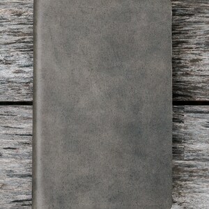 Puede incluir: Un cuaderno gris texturizado con una cubierta en blanco. El cuaderno est&aacute; sobre una superficie de madera desgastada.