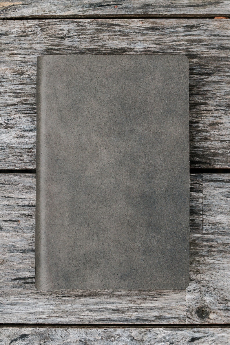 Puede incluir: Un cuaderno gris texturizado con una cubierta en blanco. El cuaderno est&aacute; sobre una superficie de madera desgastada.