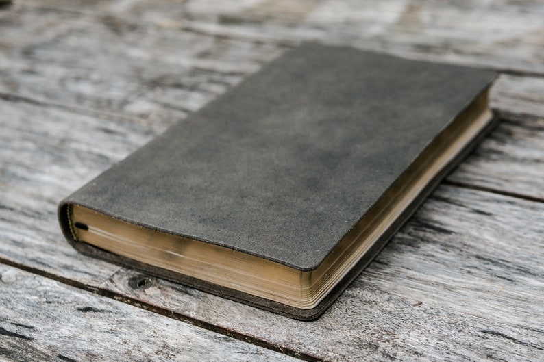 Puede incluir: Un diario de cuero gris oscuro con un borde dorado. El diario est&aacute; cerrado y acostado sobre una superficie de madera.
