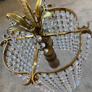 May include: A gold-toned chandelier with a crystal prism design. The chandelier has a floral-shaped top and a round, open bottom. The crystals hang in rows from the frame.