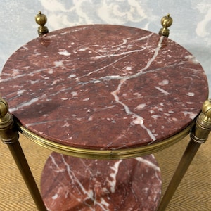 May include: A small, round side table with a red marble top and a lower shelf. The table has a brass frame and decorative finials. The marble has white veining. The table is approximately 24 inches in diameter.