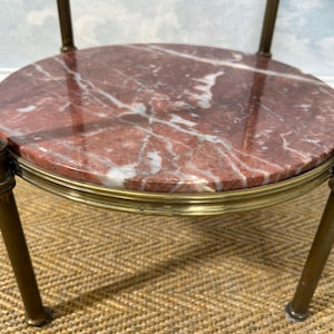 May include: A small, round side table with a red marble top featuring white veining. The table has a brass-colored metal frame and legs. The table is likely used for decorative purposes.