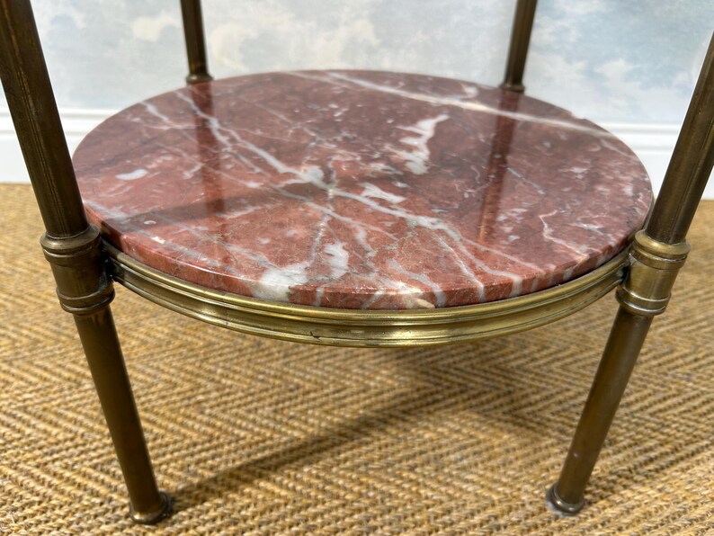 May include: A small, round side table with a red marble top featuring white veining. The table has a brass-colored metal frame and legs. The table is likely used for decorative purposes.