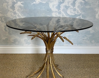 May include: A round side table with a dark glass top. The base is made of gold-colored metal, designed to resemble a bundle of wheat stalks. The table is approximately 24 inches in diameter and 20 inches tall.