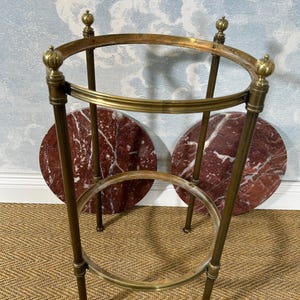 May include: A vintage brass side table with a circular top and base, supported by four slender legs. The table features two round, red marble inserts. The design includes decorative finials at the top.