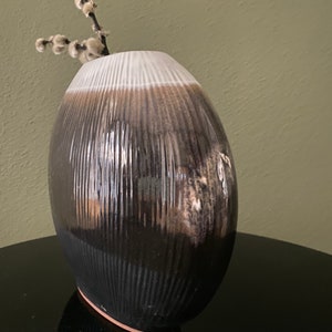 Puede incluir: Un jarrón de cerámica blanco y negro con una superficie texturizada. El jarrón tiene una forma redondeada y un borde blanco.