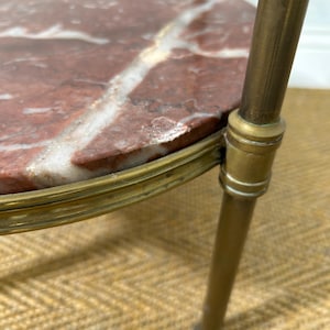 May include: Close-up of a small, round side table with a red marble top featuring white veining. The table has a brass-colored metal frame and legs. The table is a decorative piece.