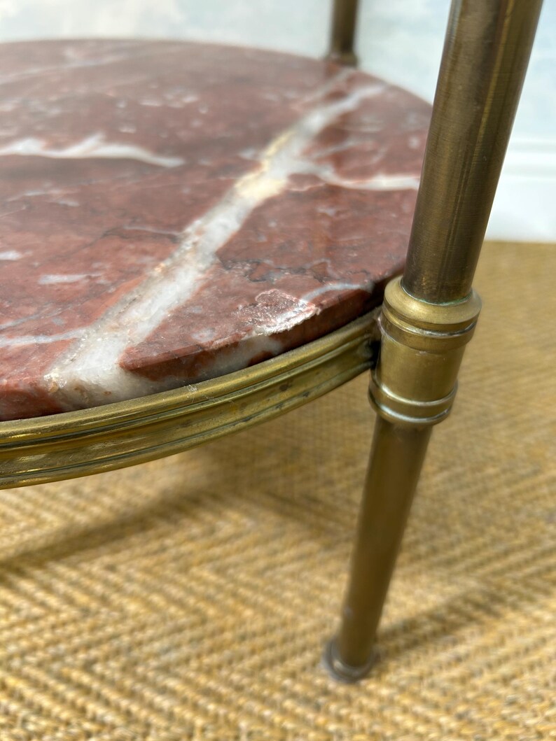 May include: Close-up of a small, round side table with a red marble top featuring white veining. The table has a brass-colored metal frame and legs. The table is a decorative piece.