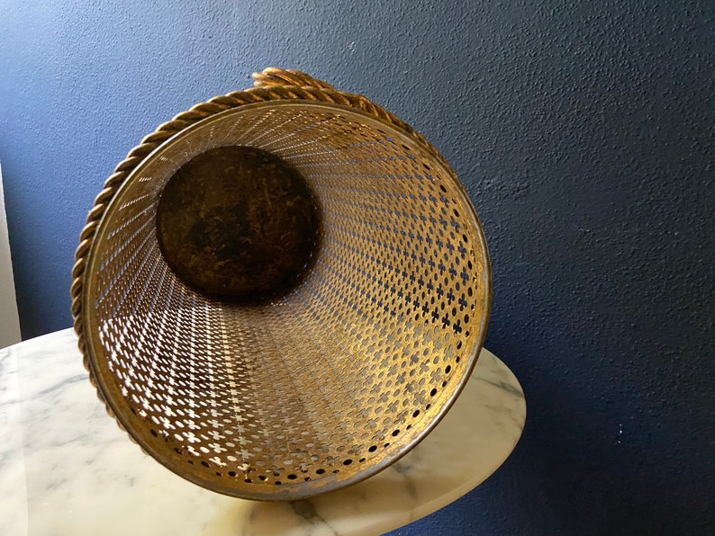 May include: Gold metal umbrella stand with a rope handle and a decorative, perforated design.