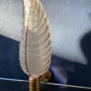 May include: A clear glass wall sconce with gold leaf detailing in the shape of a leaf. The sconce is mounted on a brass wall bracket.