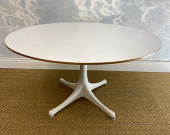 May include: White oval table with a white pedestal base and four legs. The table is on a brown woven rug.