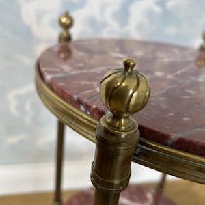 May include: A small, antique side table with a red marble top and brass accents. The table features a rounded oval top, supported by brass legs and decorative finials. The marble top has a reddish-brown color with white veining.
