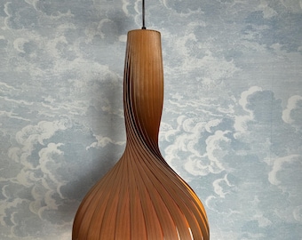 May include: A wooden pendant light fixture with a unique, curved design. The light fixture is brown and has a bulbous bottom that tapers to a narrower top. The light is suspended from the ceiling by a black cord.