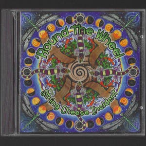 May include: CD case featuring the album "Round The Wheel" by String Cheese Incident. The artwork is a colorful, psychedelic design with a central spiral, lizards, and dragonfly illustrations. The text is in green and white.