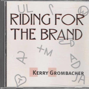 May include: A white CD case with the title "Riding for the Brand" in black text. The artist's name, "Kerry Grumbacher", is printed in black text on a pink rectangle. The case is decorated with various silver and black symbols.