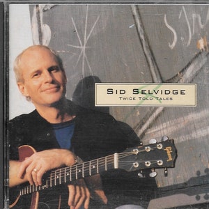 May include: A man with a guitar sits in front of a chalkboard with the text "Sid Selvidge Twice Told Tales".