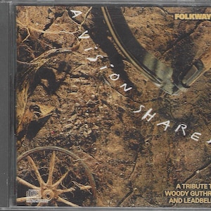 May include: A CD case with a brown and tan background image. The text "A Vision Shared" is written vertically in white on the left side of the case. The text "Folkways" is written in white on the top right side of the case. The text "A Tribute to Woody Guthrie and Leadbelly" is written in white on the bottom right side of the case.