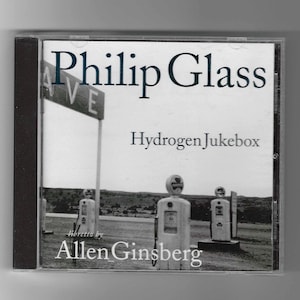 May include: A black and white photo of a CD case with a black and white photo of a gas station on the front. The text on the front of the case reads "Philip Glass Hydrogen Jukebox Libretto by Allen Ginsberg".