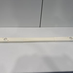 Puede incluir: Una barra de luz LED segmentada, de color blanquecino, con tres secciones. Cada sección del extremo tiene una luz circular. La barra descansa sobre una superficie blanca.