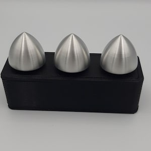 Puede incluir: Tres objetos de color plateado, puntiagudos y en forma de cúpula se muestran sobre una base rectangular negra.