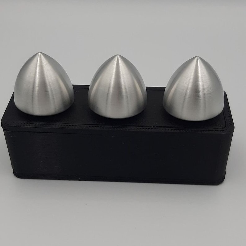 Puede incluir: Tres objetos de color plateado, puntiagudos y en forma de c&uacute;pula se muestran sobre una base rectangular negra.
