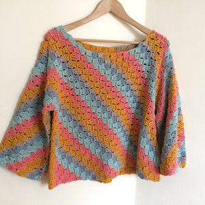 Puede incluir: Un suéter tejido a crochet con un patrón geométrico en tonos de azul, rosa y amarillo.