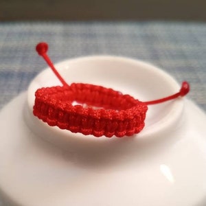 May include: A red braided string bracelet on a white ceramic dish. The dish has black writing on the bottom.