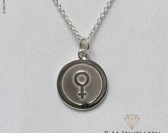 May include: A silver necklace with a round pendant featuring the female symbol. The pendant has a textured surface and a raised border.
