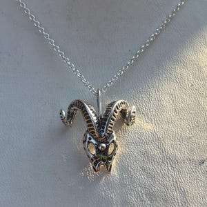 May include: Silver ram pendant necklace. The pendant depicts a detailed ram's head with curved horns and a textured surface, suspended from a delicate chain. The necklace is displayed on a white surface.