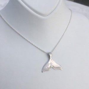 Puede incluir: Un collar de plata con un colgante de cola de ballena detallada. La cadena es delicada y el colgante mide aproximadamente 2,5 cm de largo.