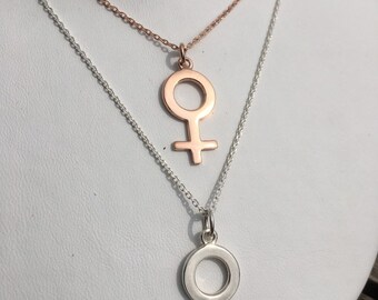 May include: Two silver chains with a pendant of the female symbol. The top chain is rose gold and the bottom chain is silver.