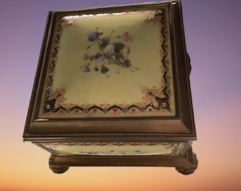 May include: A square, antique, porcelain jewelry box with a floral design. The box is decorated with gold trim and has four feet.