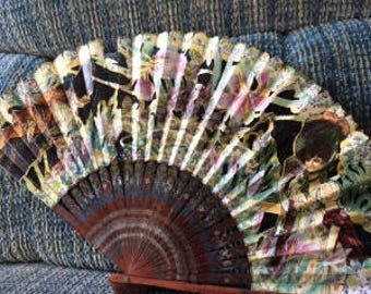 May include: A vintage hand fan with a wooden frame and a colorful floral design. The fan features a black background with pink, yellow, and green flowers and leaves.