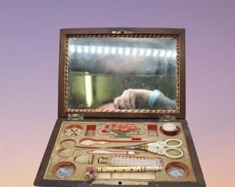 Op de afbeelding: Een antieke houten naaibox met een scharnierende spiegel en een verscheidenheid aan naai-accessoires, waaronder een schaar, naalden, draad en een vingerhoed.