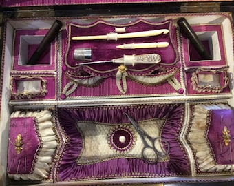 May include: An antique sewing box with a purple velvet interior. The box is divided into compartments and includes a thimble, needles, scissors, and other sewing tools.