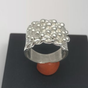 Peut inclure: Une bague en argent avec un design textur&eacute; de petites perles rondes. La bague est &eacute;paisse et large, et les perles sont dispos&eacute;es en un motif qui ressemble &agrave; une cha&icirc;ne.