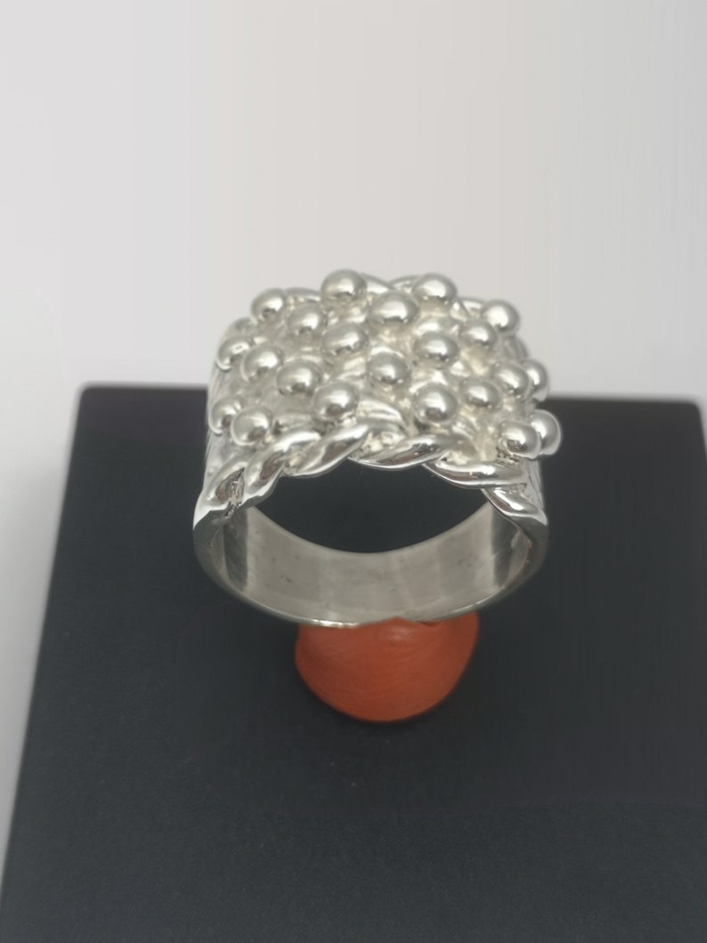 Peut inclure: Une bague en argent avec un design textur&eacute; de petites perles rondes. La bague est &eacute;paisse et large, et les perles sont dispos&eacute;es en un motif qui ressemble &agrave; une cha&icirc;ne.