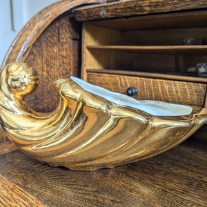 Op de afbeelding: Een gouden keramische kom met een golvend ontwerp. De kom staat op een houten oppervlak.