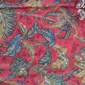 Könnte beinhalten: Roter Stoff mit einem goldenen, blauen und grünen Blumenmuster. Der Stoff hat eine strukturierte Oberfläche und ein sich wiederholendes Muster.