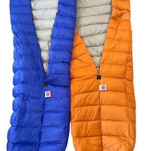 Puede incluir: Dos sacos de dormir, uno azul y otro naranja, están extendidos. Los sacos de dormir están hechos de un material acolchado y tienen una cremallera en el medio.