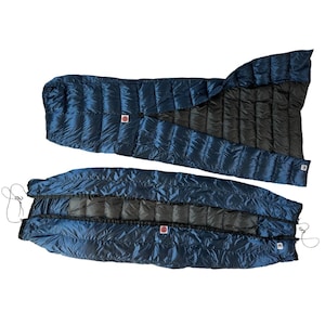 May include: A blue and black down sleeping bag with a zipper down the center. The sleeping bag is folded in half and laid out flat.