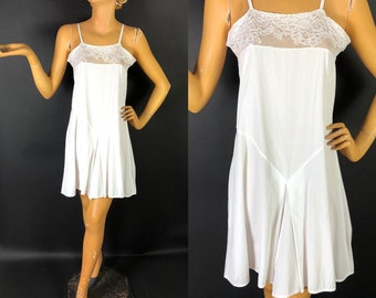 May include: White cotton slip dress with lace trim at the neckline. The dress has a fitted bodice and a flowing skirt.
