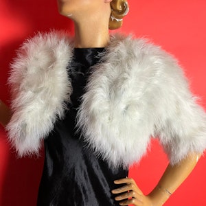 Puede incluir: Una estola de plumas blancas con mangas cortas. La estola está hecha de plumas suaves y esponjosas y es perfecta para añadir un toque de elegancia a cualquier atuendo.