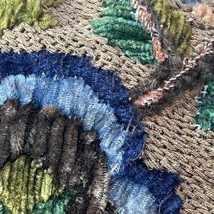 May include: Close-up of a brown fabric with blue, green, and brown embroidery. The fabric has a textured, woven appearance.