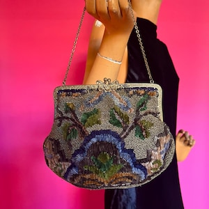 May include: A vintage beaded evening bag with a floral design in shades of blue, green, brown, and silver. The bag has a silver chain strap and a clasp closure.