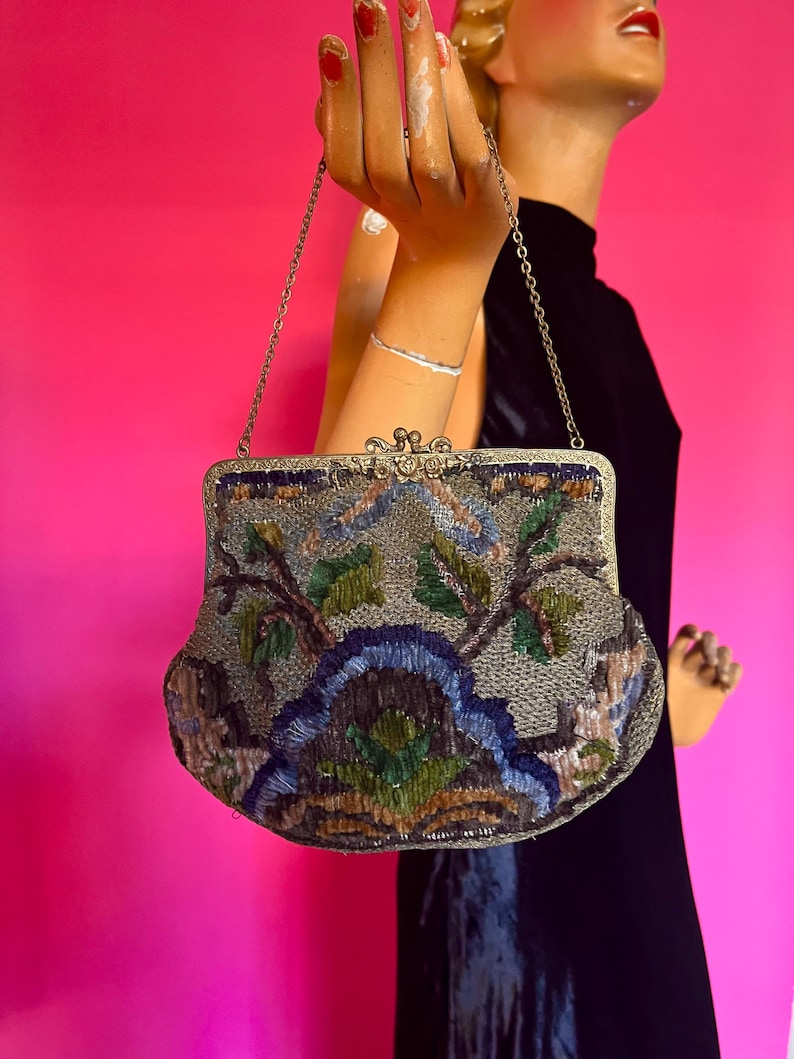 May include: A vintage beaded evening bag with a floral design in shades of blue, green, brown, and silver. The bag has a silver chain strap and a clasp closure.