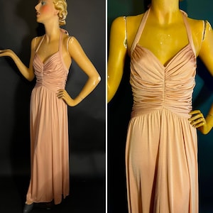 May include: A peach-colored halter-neck maxi dress. The bodice features gathered fabric, and the dress has a flowing skirt. The dress is displayed on a mannequin. The dress is a vintage style.
