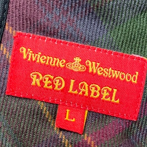 May include: Red label with the text "Vivienne Westwood Red Label" in gold lettering on a red background. The label has a small orb symbol with a crown on top. The label is attached to a plaid fabric with green, red, and black colors. The size "L" is on a smaller red label attached to the larger label.