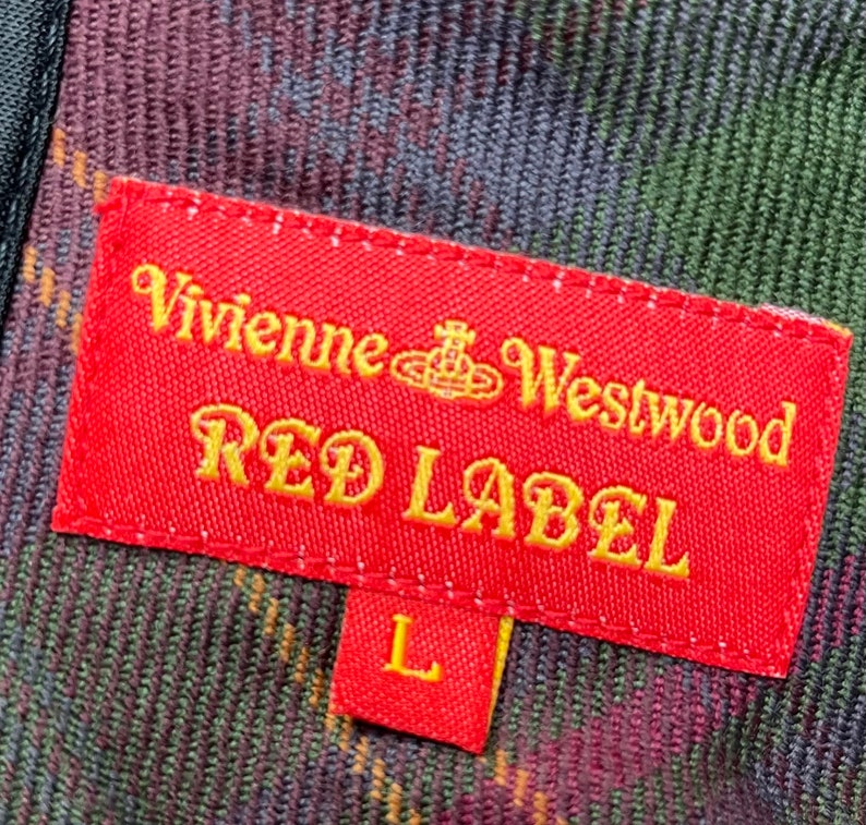 May include: Red label with the text "Vivienne Westwood Red Label" in gold lettering on a red background. The label has a small orb symbol with a crown on top. The label is attached to a plaid fabric with green, red, and black colors. The size "L" is on a smaller red label attached to the larger label.
